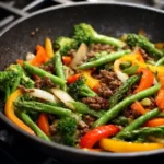 Colorful vegetables, including bell peppers, green beans, and carrots, being stir-fried in a skillet for a healthy ground beef stir fry.